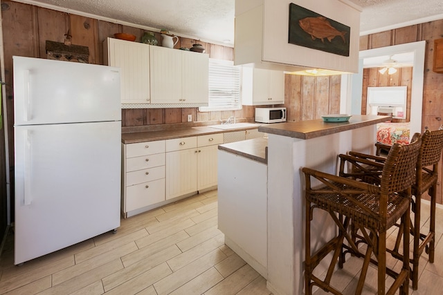 kitchen featuring wood walls, stainless steel counters, a textured ceiling, a center island, and white appliances