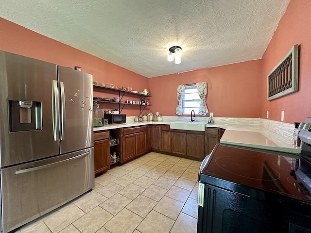 kitchen featuring electric range oven, sink, light tile patterned floors, kitchen peninsula, and stainless steel refrigerator with ice dispenser