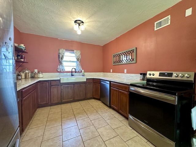 kitchen with a textured ceiling, stainless steel appliances, light stone counters, sink, and light tile floors