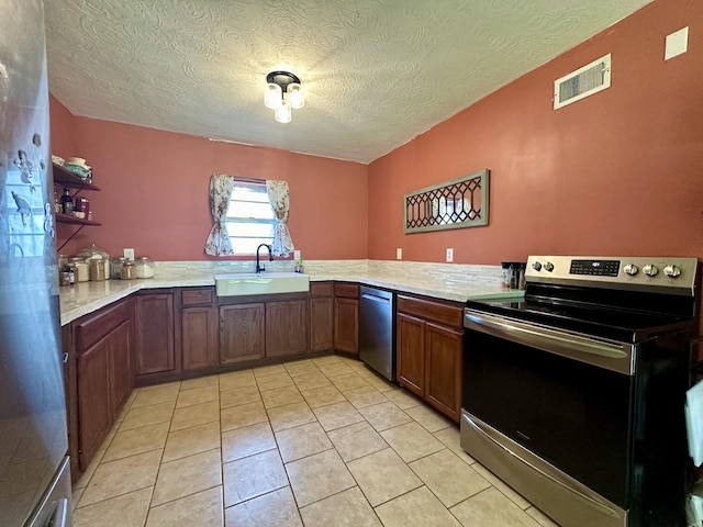 kitchen featuring sink, light tile patterned floors, kitchen peninsula, stainless steel appliances, and a textured ceiling