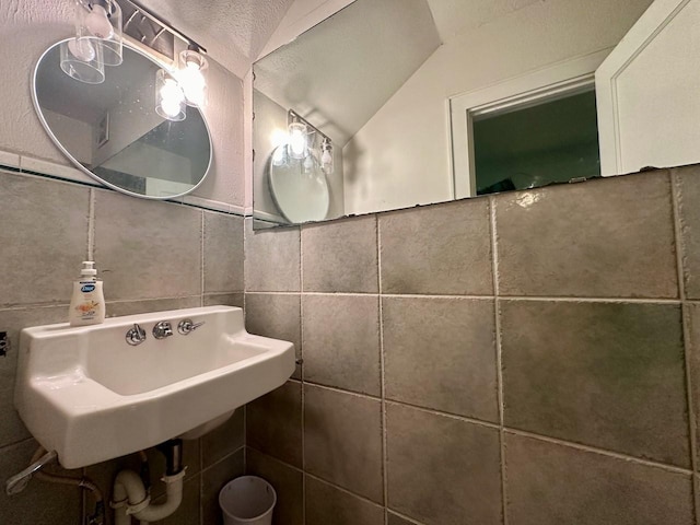 bathroom featuring vaulted ceiling, sink, and tile walls