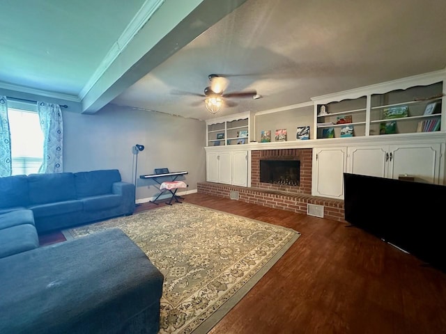 living room featuring built in features, ceiling fan, crown molding, a brick fireplace, and dark wood-type flooring