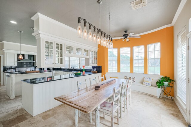 kitchen featuring wall chimney range hood, ceiling fan, kitchen peninsula, and light tile floors