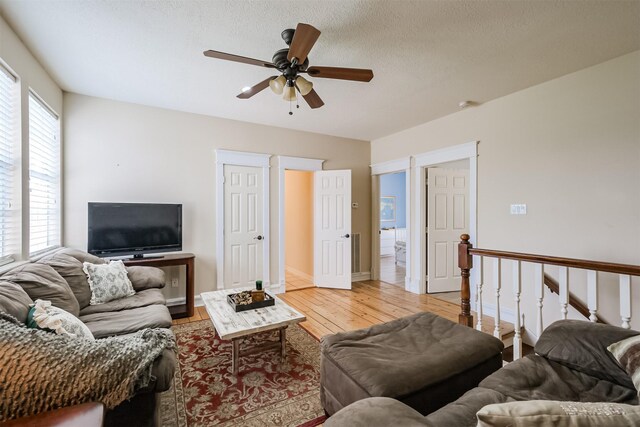 living room with a textured ceiling, ceiling fan, and light hardwood / wood-style flooring