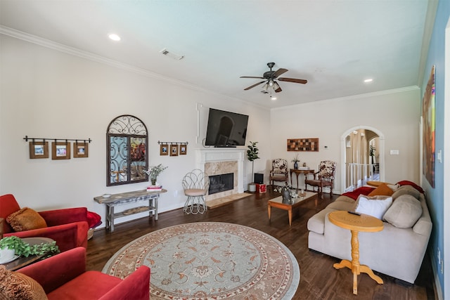 living room featuring a high end fireplace, ceiling fan, crown molding, and dark wood-type flooring