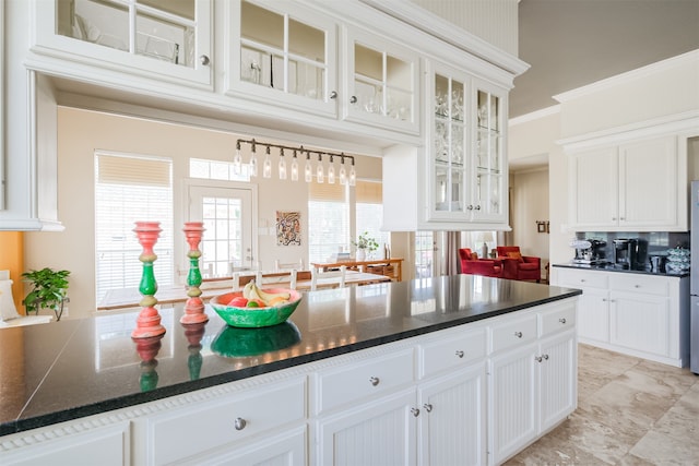 kitchen with dark stone countertops, white cabinetry, ornamental molding, and light tile floors