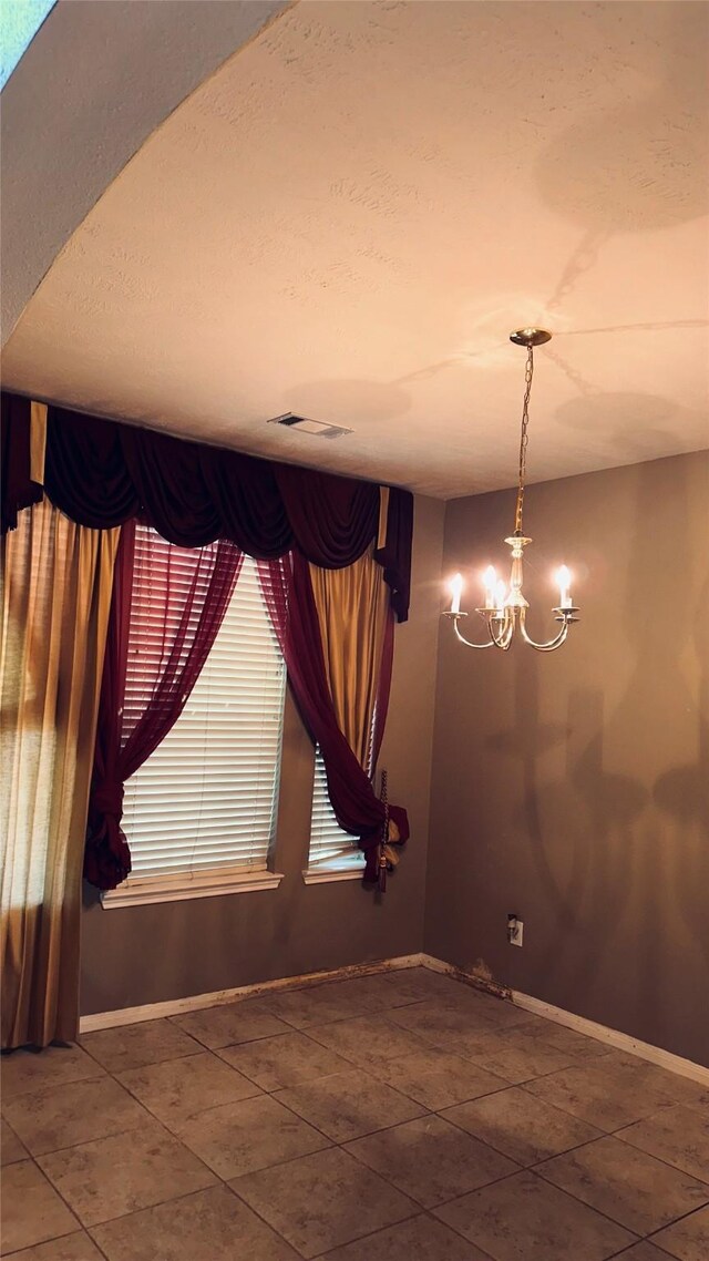 tiled empty room with a notable chandelier and a textured ceiling