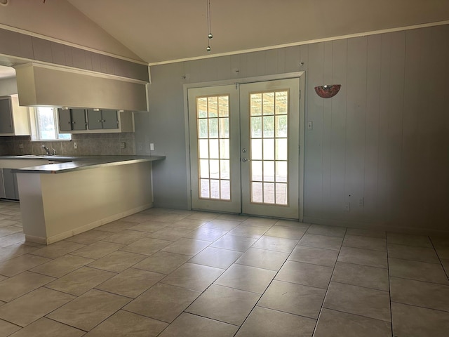 kitchen with french doors, backsplash, kitchen peninsula, lofted ceiling, and light tile patterned floors