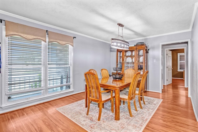 dining area with light wood-type flooring, ornamental molding, a textured ceiling, and plenty of natural light