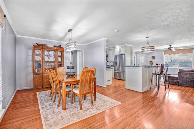 dining space with light wood-type flooring, a textured ceiling, crown molding, and ceiling fan with notable chandelier