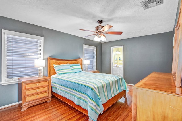 bedroom with a textured ceiling, ceiling fan, ensuite bathroom, and light hardwood / wood-style flooring