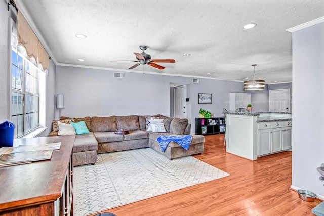 living room with light wood-type flooring, ceiling fan, ornamental molding, and a textured ceiling