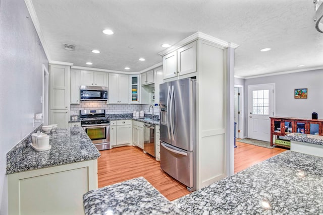 kitchen with sink, crown molding, light wood-type flooring, appliances with stainless steel finishes, and dark stone counters