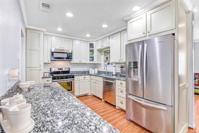 kitchen featuring white cabinetry, light hardwood / wood-style floors, appliances with stainless steel finishes, decorative backsplash, and stone countertops