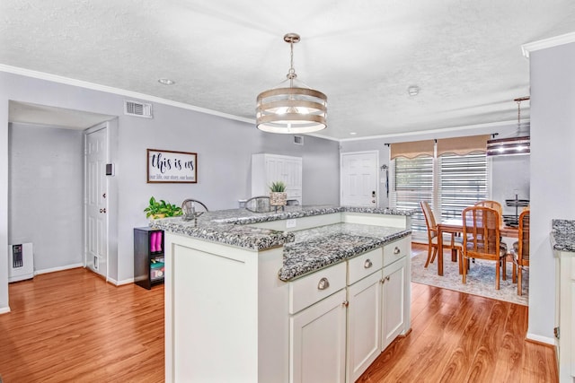 kitchen with pendant lighting, a kitchen island, crown molding, white cabinetry, and light stone countertops