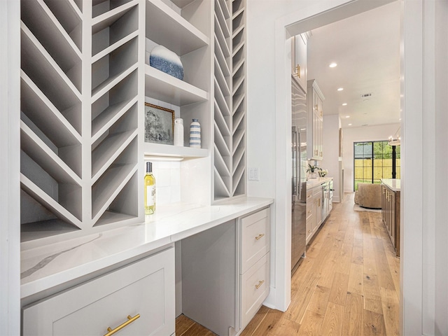 bar featuring white cabinets, high end refrigerator, light stone counters, and light hardwood / wood-style flooring