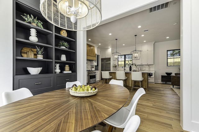 dining space with built in shelves, a notable chandelier, and light wood-type flooring