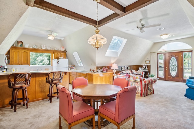 dining area featuring a textured ceiling, ceiling fan with notable chandelier, vaulted ceiling with skylight, sink, and light colored carpet