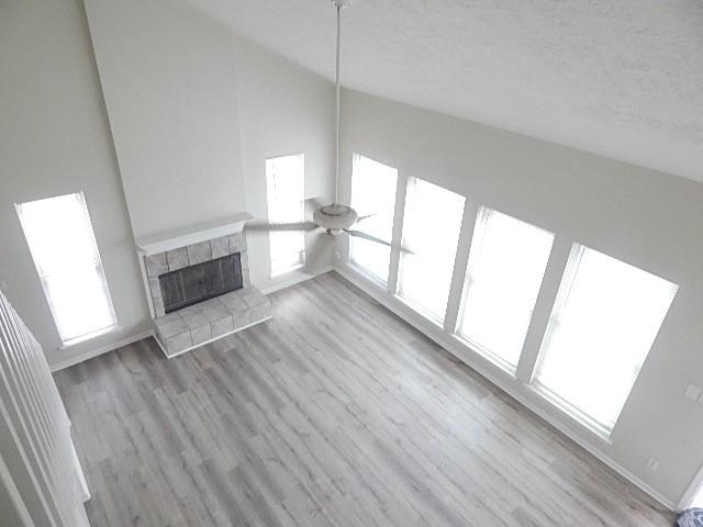 unfurnished living room featuring a tile fireplace, ceiling fan, high vaulted ceiling, a textured ceiling, and light wood-type flooring