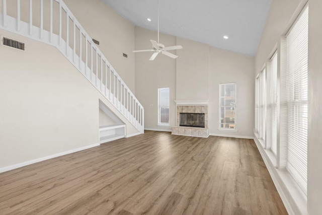 unfurnished living room with light wood-type flooring, a tiled fireplace, high vaulted ceiling, and ceiling fan