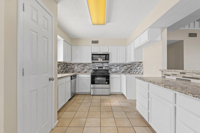 kitchen with appliances with stainless steel finishes, light tile patterned flooring, light stone countertops, and white cabinets