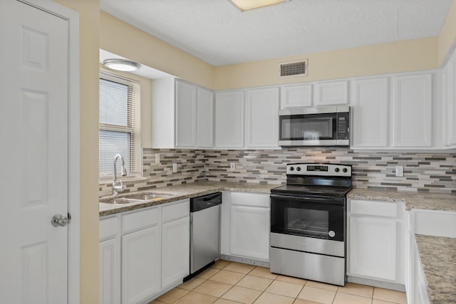 kitchen with appliances with stainless steel finishes, sink, light tile patterned floors, white cabinetry, and decorative backsplash