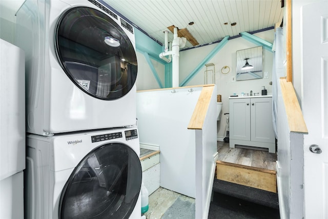 clothes washing area featuring laundry area, stacked washing maching and dryer, and wooden ceiling