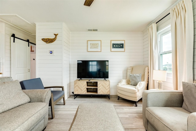 living area featuring a barn door, visible vents, ceiling fan, light wood-style flooring, and wood walls