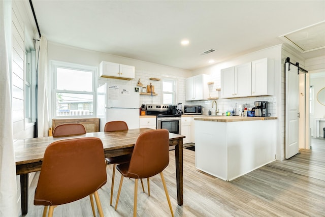 kitchen featuring a barn door, visible vents, decorative backsplash, light wood-style flooring, and stainless steel appliances