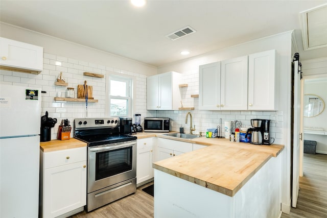 kitchen featuring light wood-style flooring, wooden counters, stainless steel appliances, open shelves, and a sink