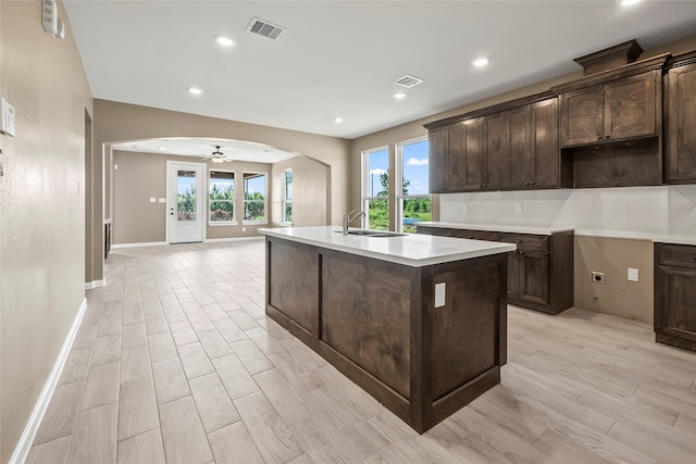 kitchen with dark brown cabinets, a kitchen island with sink, tasteful backsplash, and sink