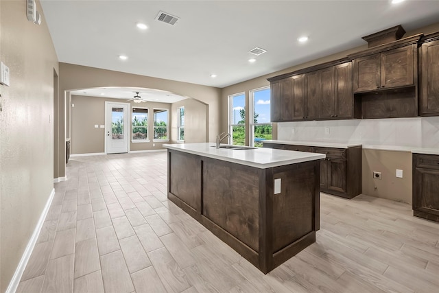 kitchen with dark brown cabinetry, sink, light hardwood / wood-style flooring, and a center island with sink