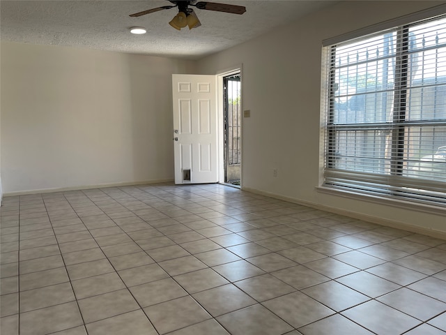 tiled empty room featuring a textured ceiling, ceiling fan, and a healthy amount of sunlight