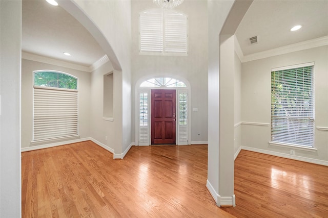 foyer with a healthy amount of sunlight, light hardwood / wood-style flooring, ornamental molding, and a notable chandelier