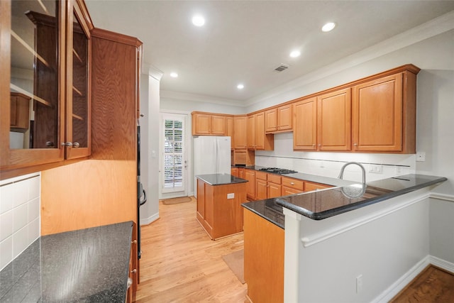 kitchen featuring backsplash, light hardwood / wood-style flooring, dark stone countertops, white fridge, and kitchen peninsula