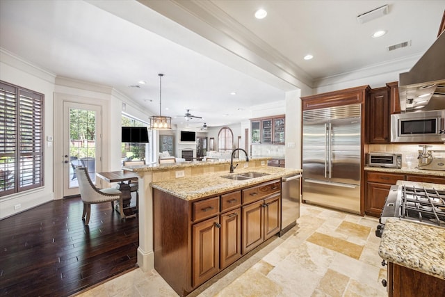 kitchen with built in appliances, ceiling fan, a center island with sink, and sink