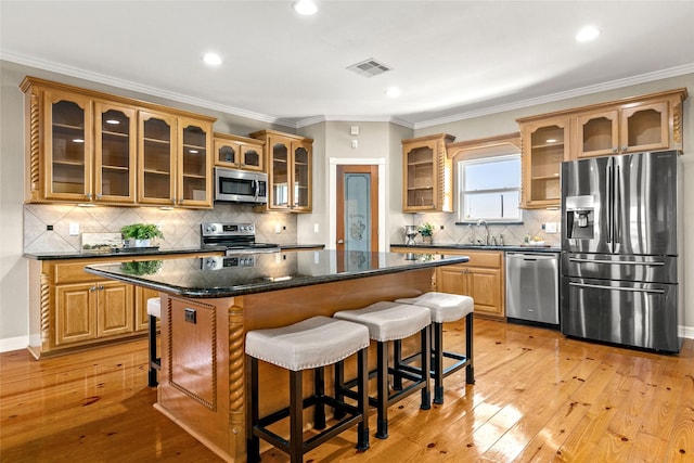 kitchen with appliances with stainless steel finishes, dark stone counters, ornamental molding, a center island, and light hardwood / wood-style floors