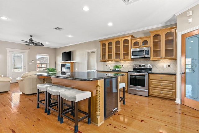 kitchen with a kitchen breakfast bar, ceiling fan, light wood-type flooring, appliances with stainless steel finishes, and tasteful backsplash