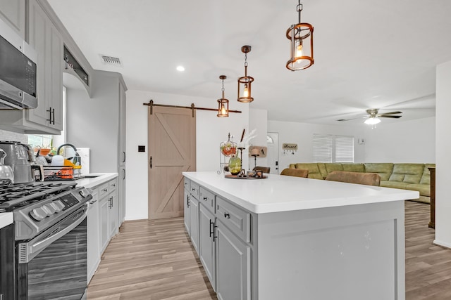 kitchen with hanging light fixtures, light hardwood / wood-style flooring, appliances with stainless steel finishes, a barn door, and ceiling fan