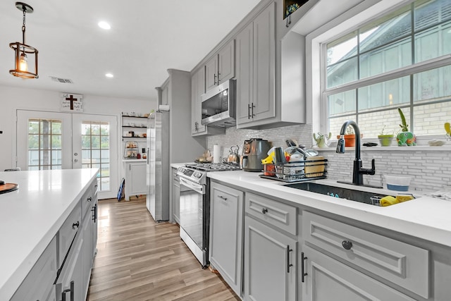 kitchen with light hardwood / wood-style flooring, backsplash, hanging light fixtures, sink, and appliances with stainless steel finishes