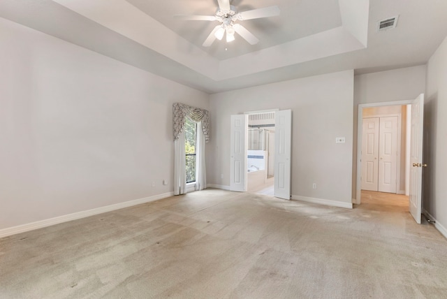 carpeted spare room with a raised ceiling and ceiling fan