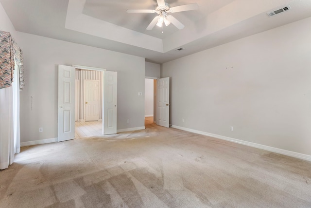 unfurnished bedroom with a raised ceiling, light colored carpet, and ceiling fan