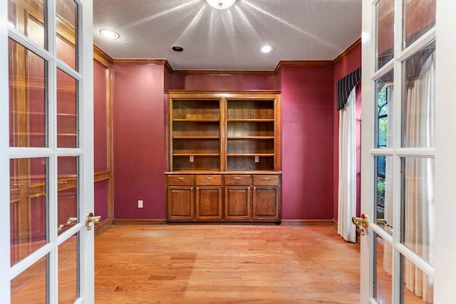 unfurnished office featuring crown molding, a textured ceiling, light hardwood / wood-style floors, and french doors