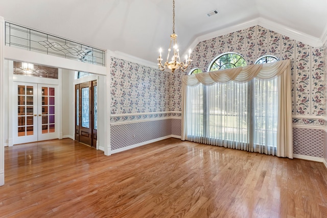 unfurnished dining area featuring french doors, ornamental molding, wood-type flooring, and a notable chandelier