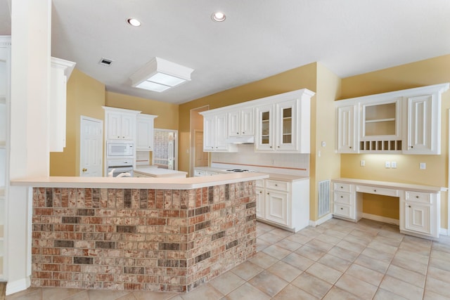 kitchen with light tile patterned floors, white appliances, built in desk, white cabinets, and kitchen peninsula