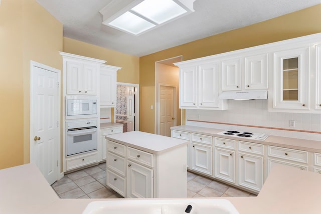 kitchen featuring light tile patterned flooring, white cabinetry, decorative backsplash, a center island, and white appliances