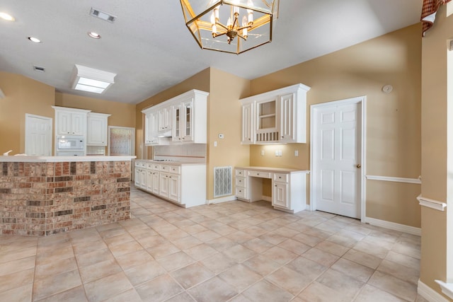 kitchen featuring built in desk, hanging light fixtures, white microwave, decorative backsplash, and white cabinets