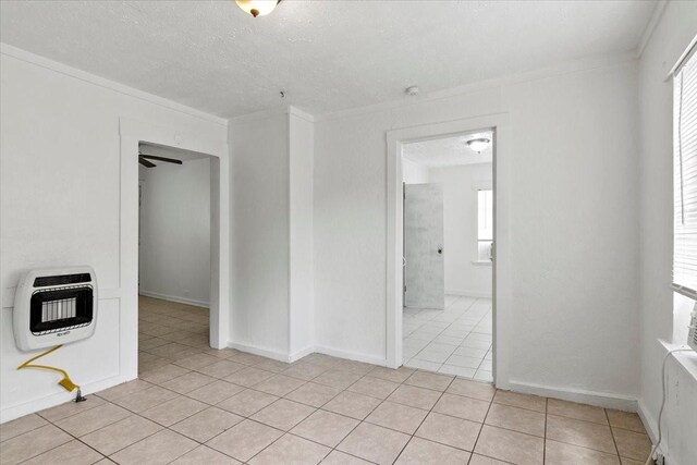 empty room featuring light tile patterned floors, a textured ceiling, baseboards, heating unit, and crown molding