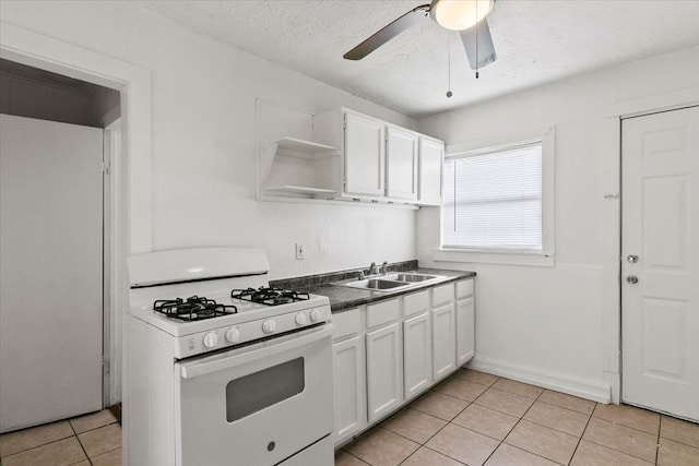 kitchen with ceiling fan, white range with gas stovetop, light tile floors, sink, and white cabinetry