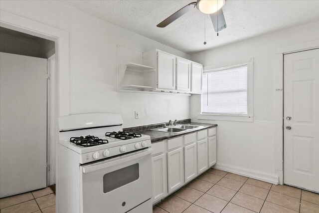 kitchen with white gas range oven, white cabinets, dark countertops, open shelves, and a sink